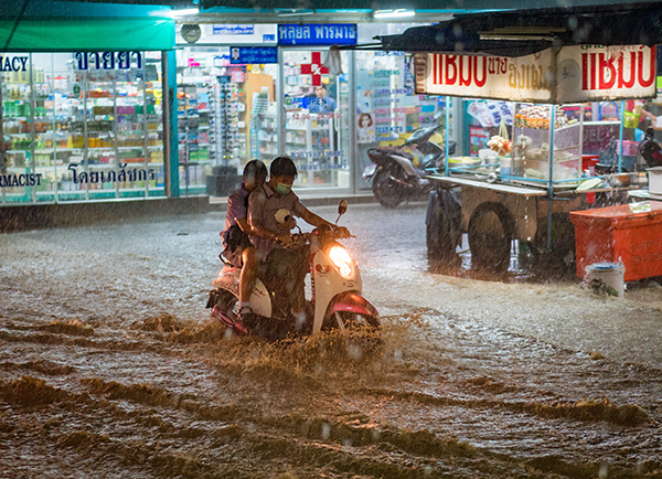 Two persons on a moped trying to ride in a flooded street